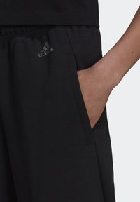 Černé sportovní šortky vyrobené z měkké látky, s elastickým pasem, bočními kapsami a duhovým logem Adidas na levé straně.