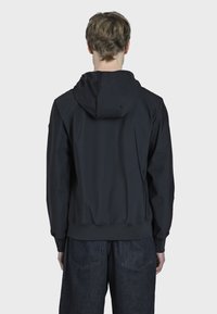 Černá kapucňová bunda vyrobená z lehkého materiálu. Má volný střih, žebrovaný lem a hladkou texturu. Zadní pohled ukazuje minimální detaily.