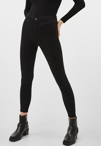 Czarne skórzane rurki z denimu, o gładkiej fakturze, wysokim stanie i klasycznym zapięciu na guzik, zestawione z botkami za kostkę.