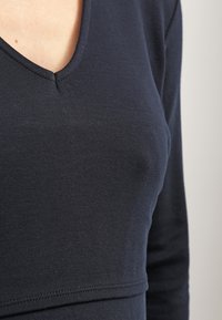 Tmavě námořnická dlouhá halenka s designem do V. Měkká, hladká tkanina s jemnou texturou a prošívaným lemem pod prsy.