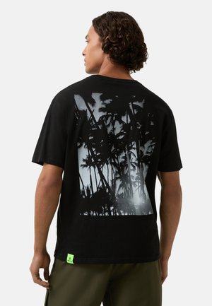 Sort bomuld t-shirt med et stort monokromt palmetræ-grafik på bagsiden og et lille lysegrønt mærke ved kanten.