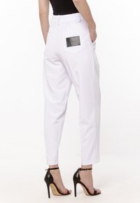Białe zwężające się spodnie z elastycznym pasem, z czarną skórzaną naszywaną kieszenią z tyłu i gładką teksturą. Noszone z czarnymi szpilkami.