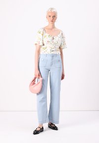 Top floreale con maniche puff, jeans a gamba larga blu chiaro, borsa rosa e ballerine nere con accenti bianchi. Tessuti lisci e colori tenui.