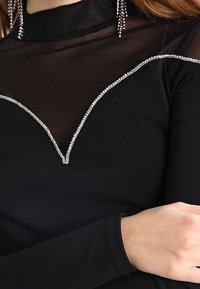 Czarna bluzka z długim rękawem i przezroczystym dekoltem, z V-kształtnym wzorem ozdobionym małymi cyrkoniami wzdłuż krawędzi.