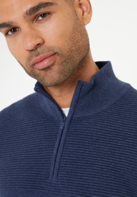 Marineblaues Zip-Up-Pullover mit gerippter Textur, ausgestattet mit einem Stehkragen und einem halblangen Reißverschluss, aus weichem Stoff gefertigt.