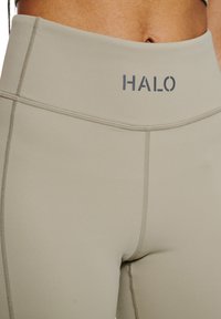 Höga beige leggings med en slät yta, tonala sömmar och en "HALO"-logotyp i mörkgrått på midjebandet.