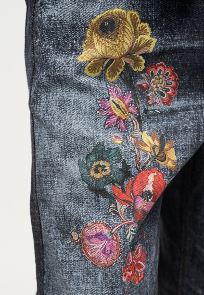 Tissu en denim avec des motifs floraux brodés colorés comprenant des fleurs jaunes, rouges, roses et vertes le long d'une tige courbée.