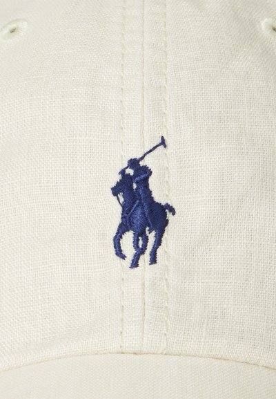 Medvilninis kepurė off-white spalvos su tamsiai mėlynu siuvinėtu polo žaidėjo logotipu. Savybės: išlenktas kraštas ir tekstūruota medžiaga. Matomų metalinių detalių nėra.