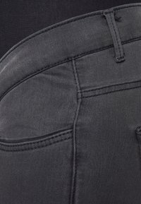 Jeans de denim negro con una textura suave, que cuentan con una cintura alta, bolsillos traseros y delicados detalles de costura.