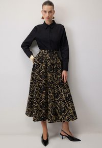 Črna bluza z dolgimi rokavi in ovratnikom, v kombinaciji z zlato vzorčasto polno črno krilo. Dodatki vključujejo zlat zapestnik in črne visoke pete.