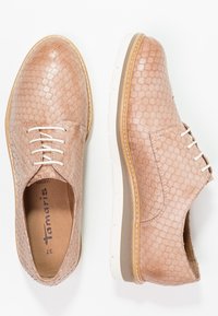 Chaussures en cuir beige avec un motif texturé rappelant la peau de reptile, bout rond, lacets blancs, et une semelle en caoutchouc agrémentée d'un accent marron clair.