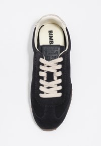 Zapatillas de ante negro con cordones en color crema, lengua texturizada con logotipo y suela de goma marrón. Diseño clásico con bordes festoneados.
