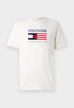 White cotton t-shirt featuring a navy and red graphic with "HILFIGER," a flag design, and "ESTABLISHED 1985" text. Classic crew neckline.