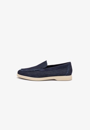 Mocasín azul marino sin cordones con suela beige clara, hecho de tela vaquera con costuras visibles y puntera redondeada, vista de perfil lateral.