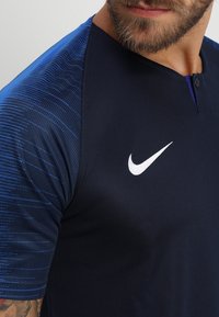 Námořnický sportovní dres s modrým texturovaným gradientem, malým límcem a výrazným bílým logem Nike na hrudi.