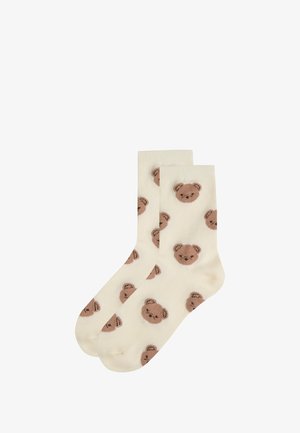 Calcetines de color crema con una textura suave, que presentan un patrón repetido de ositos de peluche marrones. Diseño cómodo y casual.