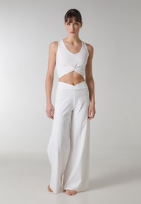 Top corto bianco con dettaglio anteriore a torsione abbinato a pantaloni bianchi ampi e fluidi. Tessuto morbido e design senza cuciture creano un aspetto liscio.