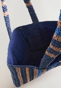 Sac cabas tissé rayé bleu et beige avec doublure en tissu bleu marine, poche intérieure et anses tissées assorties.