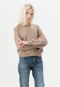 Beżowy sweter z dzianiny z okrągłym dekoltem, w luźnym fasonie, z prążkowanymi mankietami, w połączeniu z niebieskimi dżinsami. Miękka tekstura i swobodny krój.