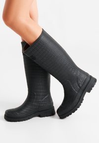 Stivali neri in gomma alti fino al ginocchio con una texture a motivo coccodrillo, suola resistente e parte superiore rinforzata per garantire durata.