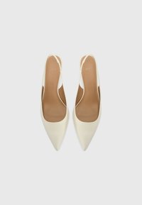 Des chaussures slingbacks à bout pointu en cuir crème au toucher lisse, avec un dos ouvert et un design minimaliste. Semelle intérieure brune visible.