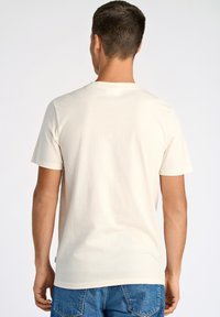 T-shirt in cotone beige chiaro con maniche corte, colletto rotondo e design semplice. Il retro è liscio con uno stile minimalista.