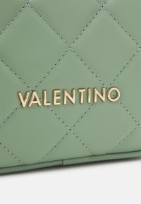 Green quilted leather bag featuring gold "VALENTINO" logo, prominent stitching detail, and a smooth texture overall.
