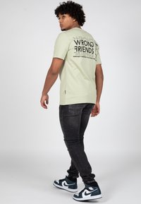 Světle zelené bavlněné tričko s černým grafickým textem na zadní straně. V kombinaci s tmavými džíny a modro-bílými vysokými teniskami.