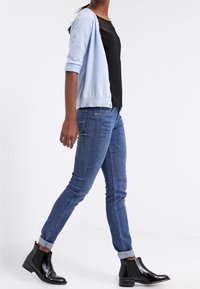 Ljusblå cardigan över en svart topp, matchad med figurvänliga blå jeans och svarta ankelstövlar. Släta texturer, avslappnad design och uppvikta ärmslut.