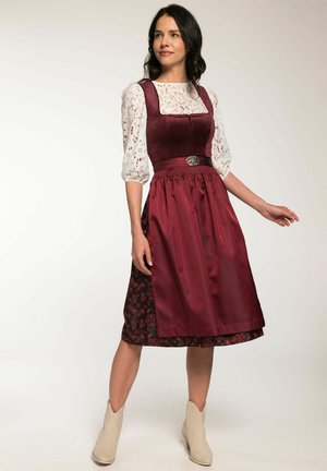 Dirndl bordeaux avec un décolleté carré, blouse en dentelle blanche, jupe à motifs floraux, et quincaillerie décorative en argent ; présente une taille ajustée.