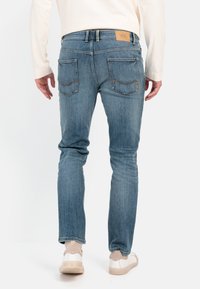 Lyst blå denimjeans med slim fit, to baglommer med buet stikning, og et lædermærke på taljebåndet.