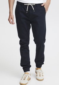 Navy jogger pants made from soft fabric, featuring an elastic waistband with a drawstring and cuffed hems. Paired with white sneakers.