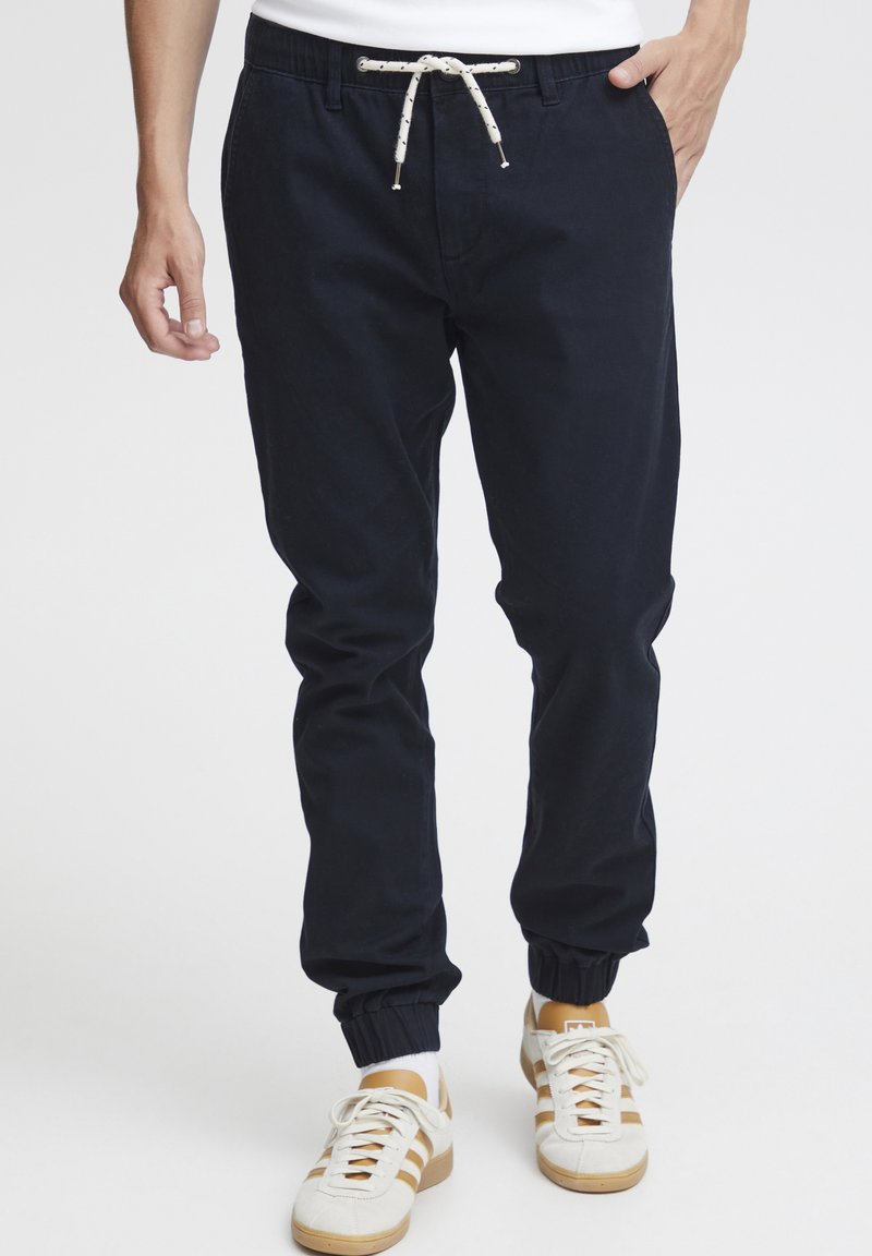 Navy jogger pants made from soft fabric, featuring an elastic waistband with a drawstring and cuffed hems. Paired with white sneakers.