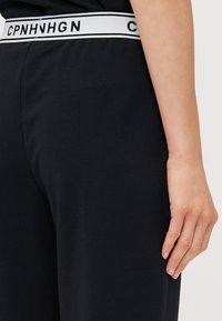 Zwarte katoenbroek met een witte elastische tailleband met merk, waarop tekst staat. De stof lijkt zacht en glad met een aansluitend ontwerp.