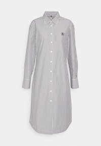 Abito bianco a maniche lunghe, lungo fino al ginocchio, con sottili righe verticali nere e bottoni bianchi sul davanti.