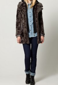 Abrigo gris de piel sintética con capucha, superpuesto a una camisa de mezclilla azul claro. Combinado con jeans azul oscuro y botas negras con cordones.