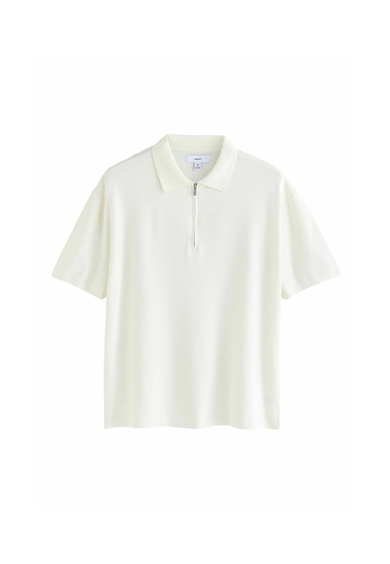 Camiseta polo en amarillo pálido, de mangas cortas, hecha de un tejido suave y texturizado, presenta un cierre de media cremallera en el frente y un diseño de cuello clásico.