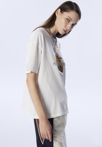 T-shirt bianco in cotone a maniche corte, con una stampa grafica di formaggio in tonalità marroni e grigie. Abbinato a pantaloni con motivo testurizzato.
