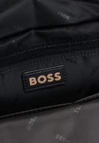 Czarny wnętrze torby z prostokątną skórzaną metką z napisem "BOSS" w jasnobrązowym kolorze. Widoczna gładka, teksturowana podszewka.