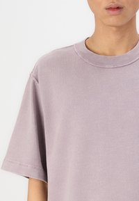 Light lavender short-sleeve T-shirt in soft cotton with a ribbed crew neckline and relaxed fit. Features minimal stitching details.