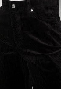 Zwarte corduroy broek met een verticale ribbelstructuur, klassieke vijf-pocket ontwerp en metalen knoopsluiting met merkdetail.