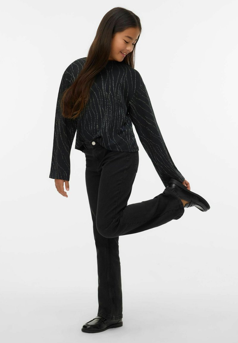Juodas ilgomis rankovėmis viršus su tekstūruotomis sidabrinėmis linijomis, derinamas su juodais džinsais ir lygiu juodu avalynu. Modelis pozuoja pakėlęs vieną pėdą.