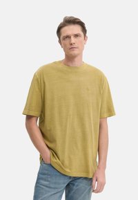 Camiseta de algodón verde oliva con cuello redondo, mangas cortas y un corte relajado. Presenta un sutil logotipo en el pecho.