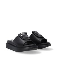 Sorte slide-sandaler har en perforeret overdel og en rund metallic udsmykning på remmen, sat mod en hvid baggrund.