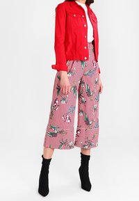 Röd jeansjacka över en vit topp, i kombination med rosa randiga vida byxor med blommiga och tropiska mönster. Bärs med svarta ankelstövlar.