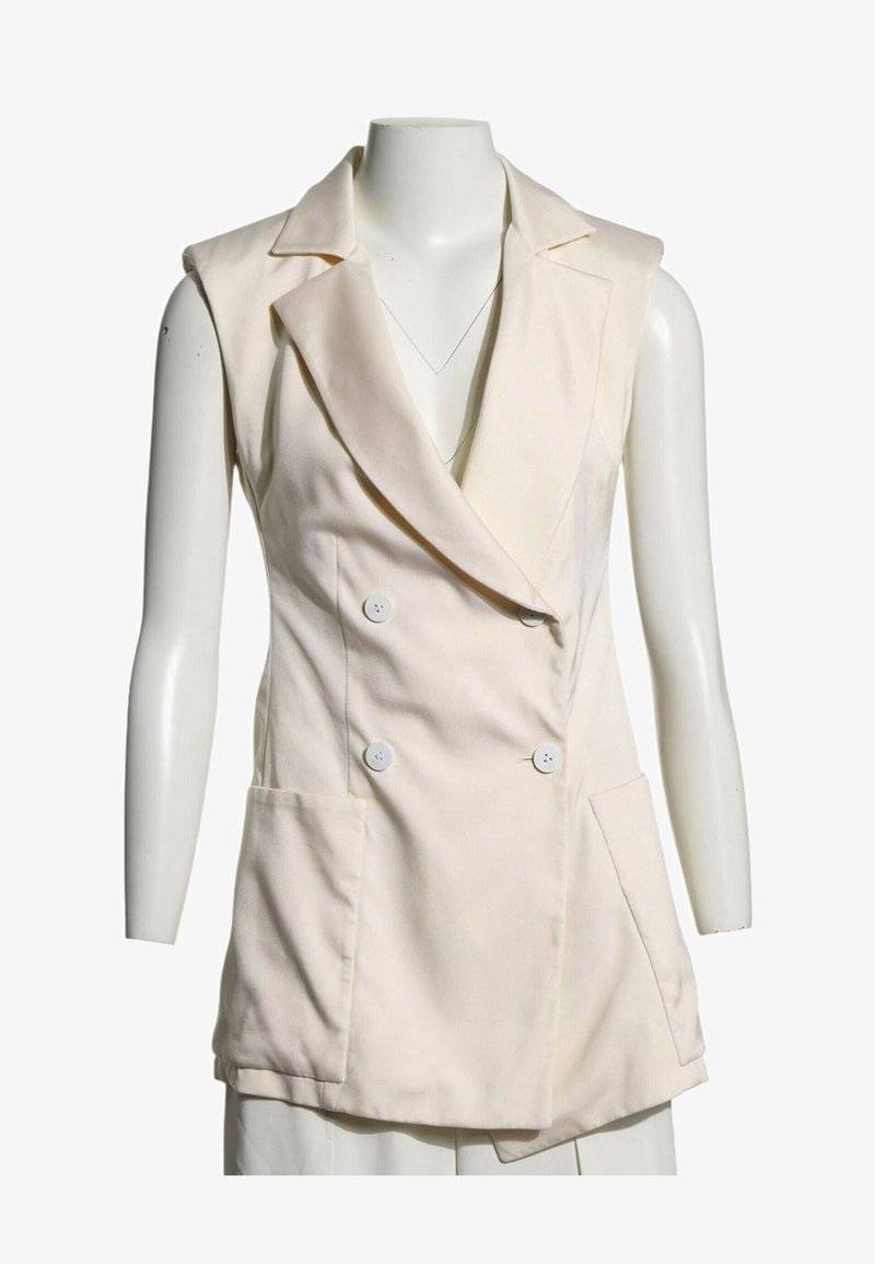 Blazer crème sans manches à double boutonnage avec larges revers et deux poches avant, présenté sur un mannequin blanc.