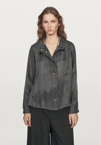 Gray, satin shirt with a snap-button closure, pointed collar, long sleeves, and a relaxed fit, featuring a slightly shiny texture.