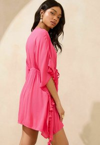 Vestito leggero rosa con una vestibilità rilassata, caratterizzato da dettagli laterali con frange, maniche kimono e una vita arricciata per una vestibilità regolabile.