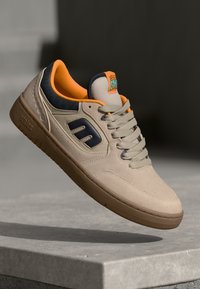 Beżowe zamszowe sneakersy z pomarańczowymi detalami, granatowymi akcentami i gumową podeszwą. Posiadają logo na języku, teksturowane panele i sznurowadła.