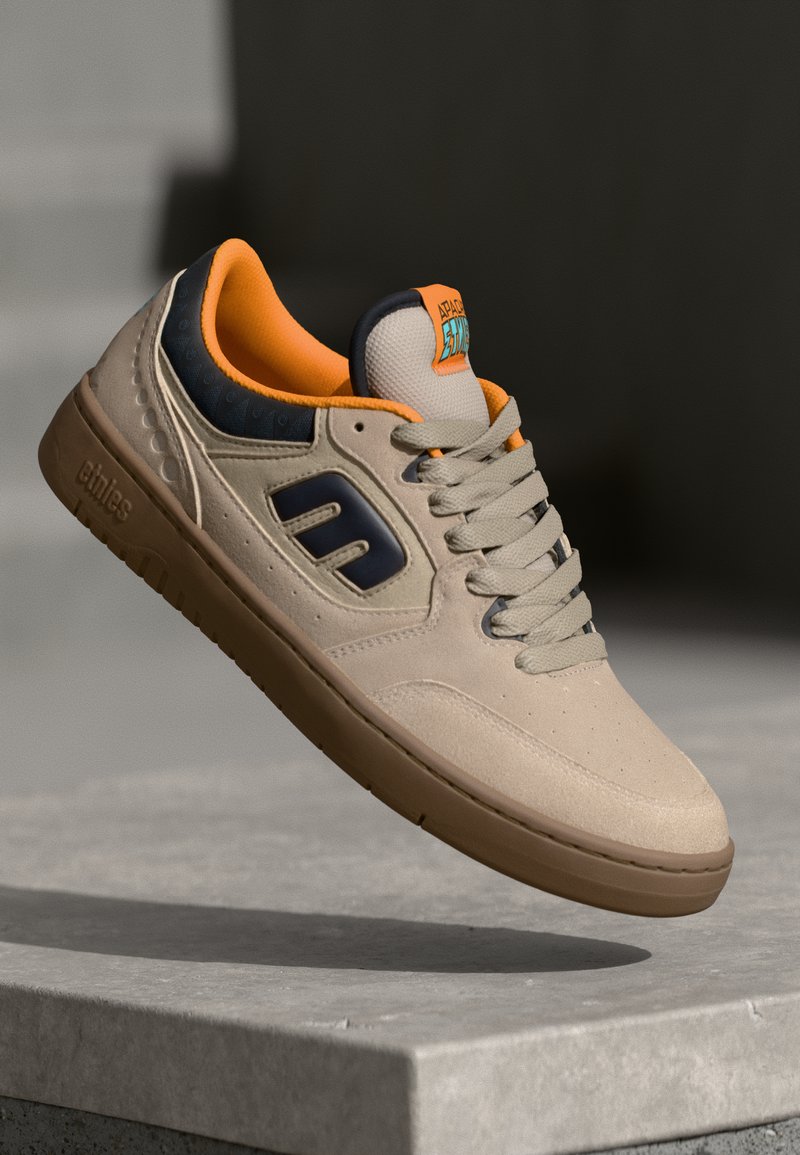 Beżowe zamszowe sneakersy z pomarańczowymi detalami, granatowymi akcentami i gumową podeszwą. Posiadają logo na języku, teksturowane panele i sznurowadła.
